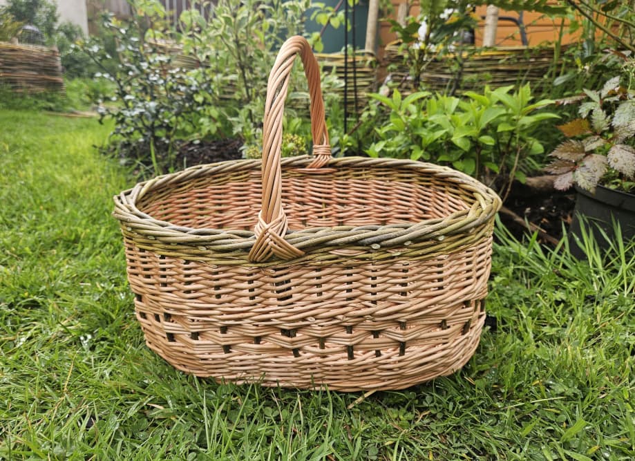 Oval willow basket with a tall handle in a garden