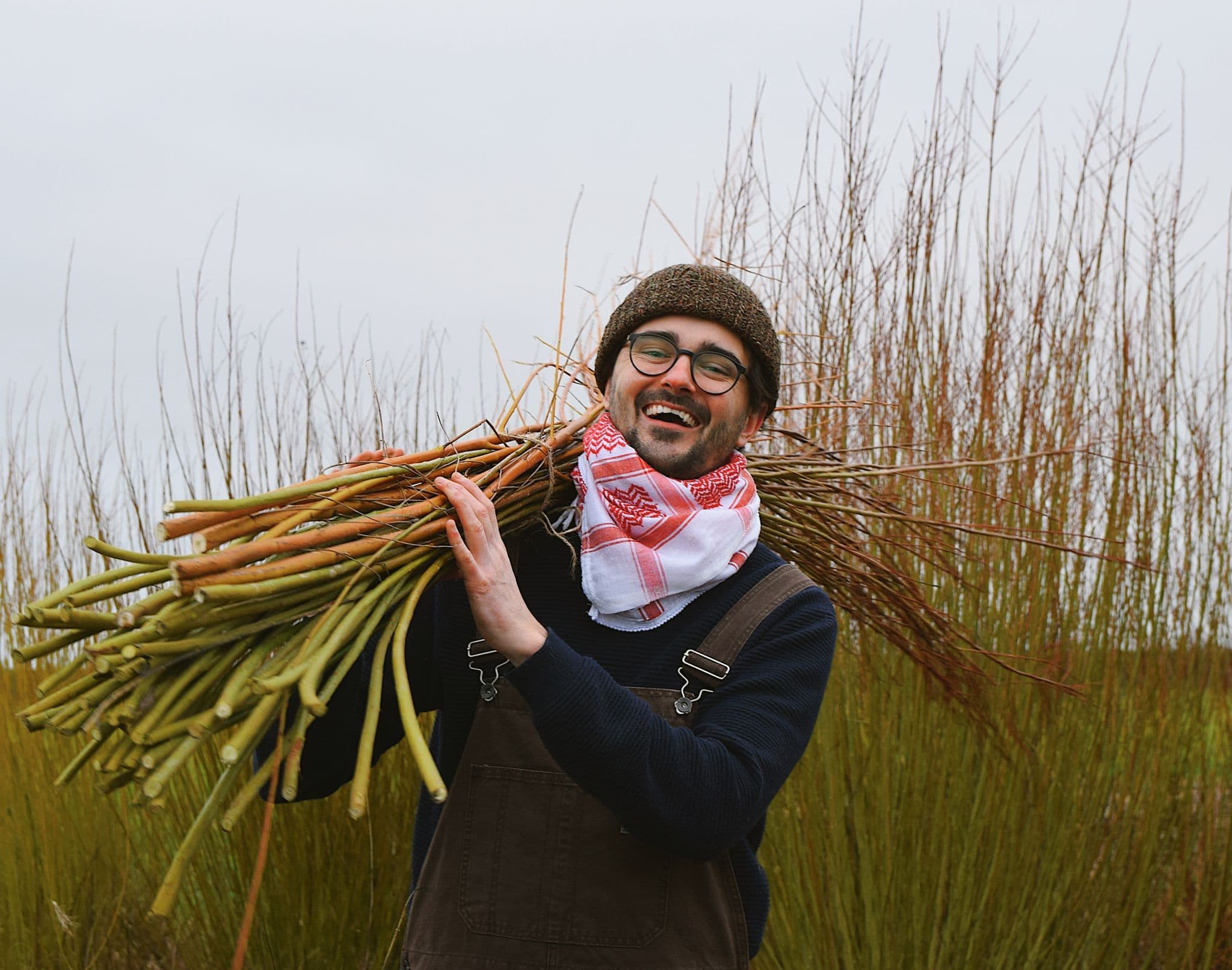 Alexander carrying a bundle of willow on his shoulder in the willow beds